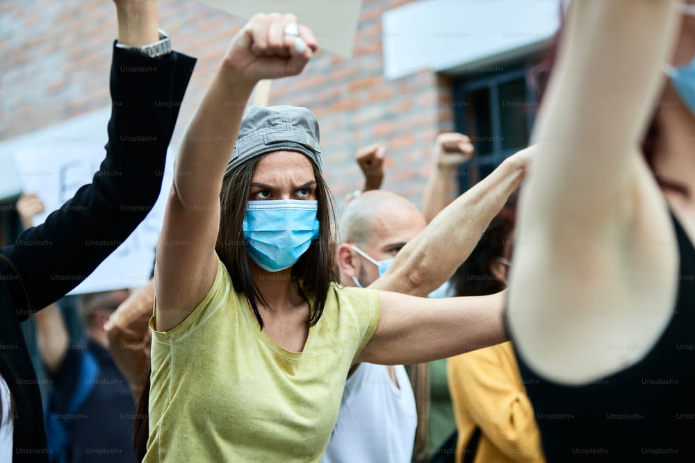 COVID-19 대유행 기간 동안 군중과 함께 항의하는 동안 보호용 안면 마스크를 착용한 여성 활동가.