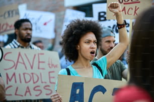 Mujer afroamericana disgustada protestando con una multitud de personas y gritando con el puño en alto.