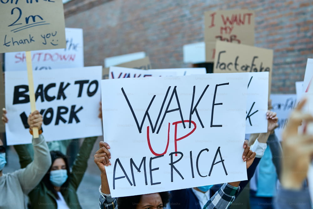コロナウイルスの流行中の抗議行動で目覚めのアメリカの碑文が入ったプラカードを持っている人のクローズアップ。