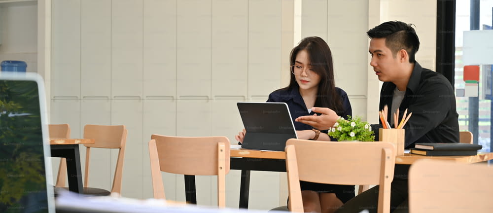 Um empresário está ensinando um novo funcionário com um tablet de computador na mesa de trabalho de madeira.