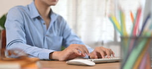 Uma imagem recortada de um homem inteligente está usando um teclado e mouse na mesa de trabalho de madeira.