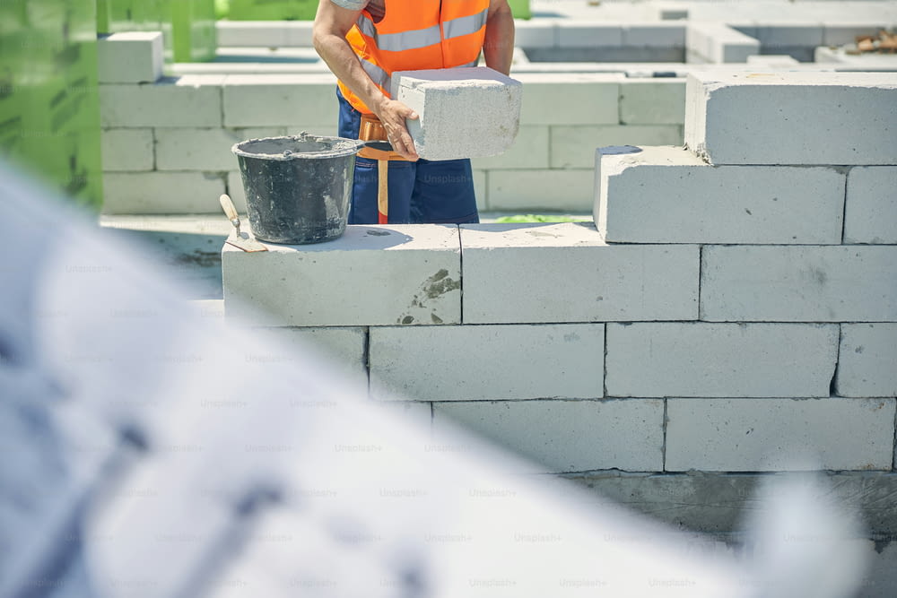 Cropped photo of a fit Caucasian male worker holding a white brick in his hands