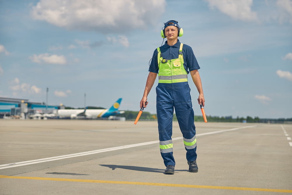 Full-sized portrait of a serious aircraft marshaller with wands walking alone across the airfield
