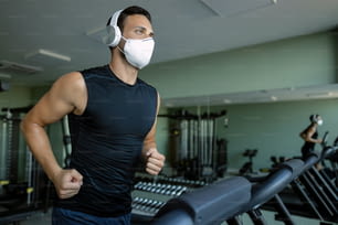 Junger Sportler trägt eine Gesichtsmaske beim Laufen auf dem Laufband im Fitnessstudio während der Coronavirus-Epidemie.
