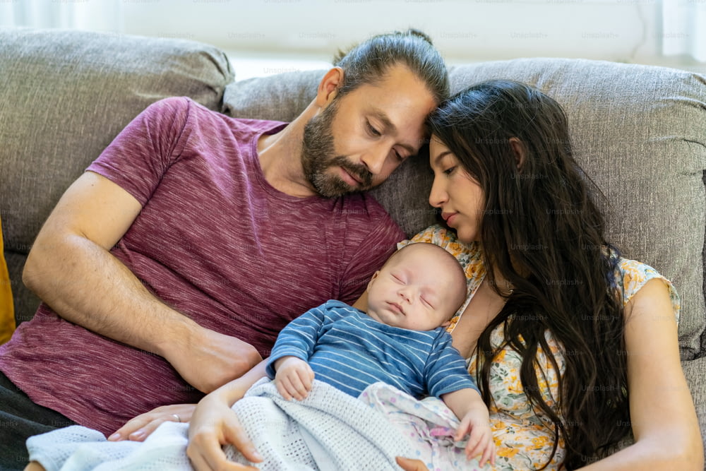 Família feliz dois pais com bebê recém-nascido descansando juntos no sofá na sala de estar