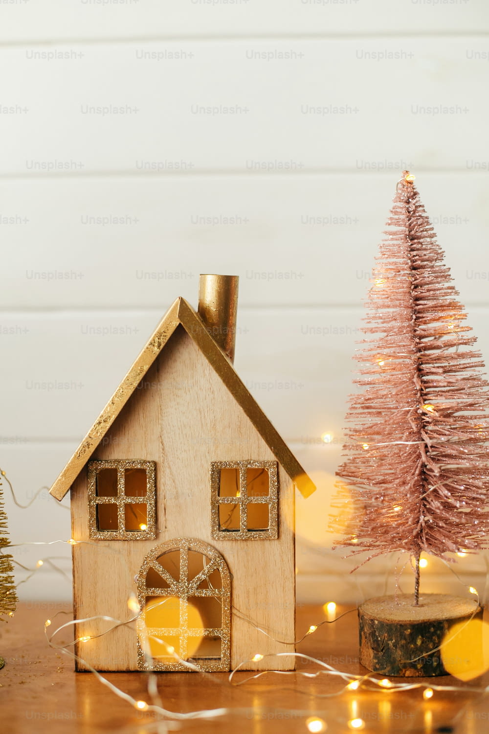 Elegante casa de navidad y árbol de navidad brillante en luces doradas. Decoración festiva moderna en la habitación escandinava. Pueblo en miniatura con casa de madera y juguetes de árbol. Feliz Navidad