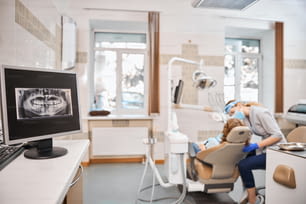 Foto de un consultorio dental con todo el equipo y aparatos dentales y una gran radiografía en la pantalla de la computadora