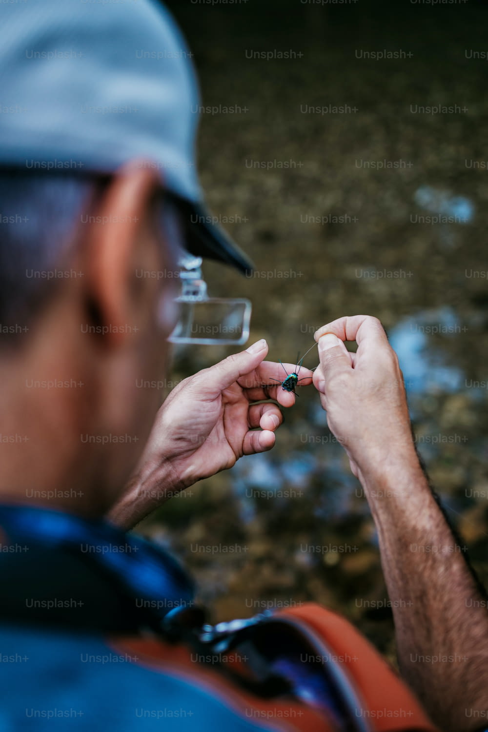 Close up tiro das mãos de pescadores seniores amarrando uma mosca para a pesca. Conceito de pesca com mosca. Vista de cima. Visão de ângulo alto sobre o ombro.