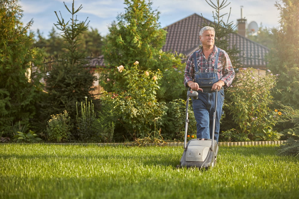 잔디 깎는 기계를 사용하여 잔디밭의 잔디를 다듬는 노인의 전체 길이 사진