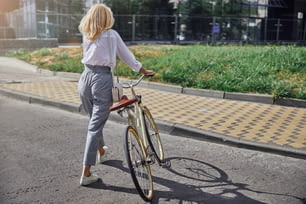 Back view portrait of woman tourist with retro city bicycle walking on the city street in the sun shine day