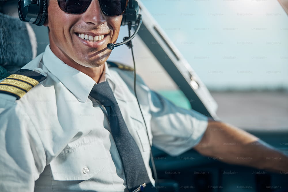 Cropped head portrait of cheerful handsome man in professional headphones sitting at control in cockpit
