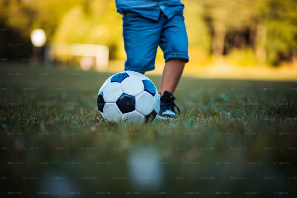 Legs of little boy playing football on grass. Close up.