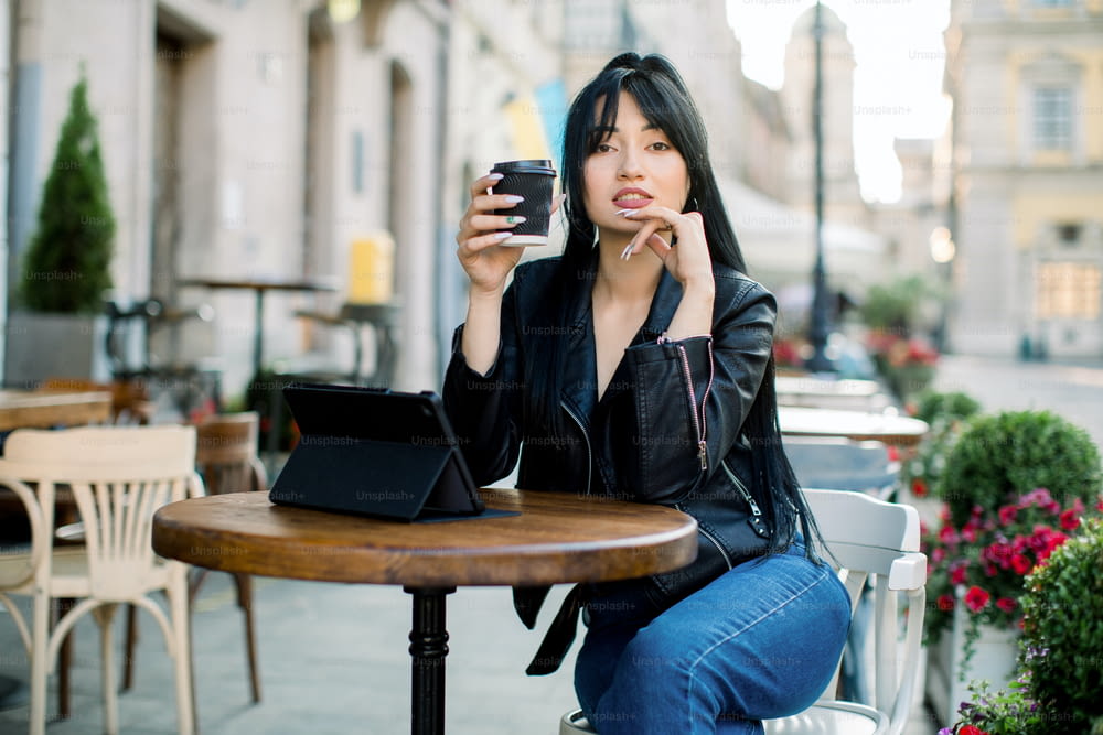 Lifestyle freelance concept. Pretty working young Asian woman with tablet computer, drinking coffee in outdoor city coffee cafe shop, working online, reading news and enjoying coffee break.