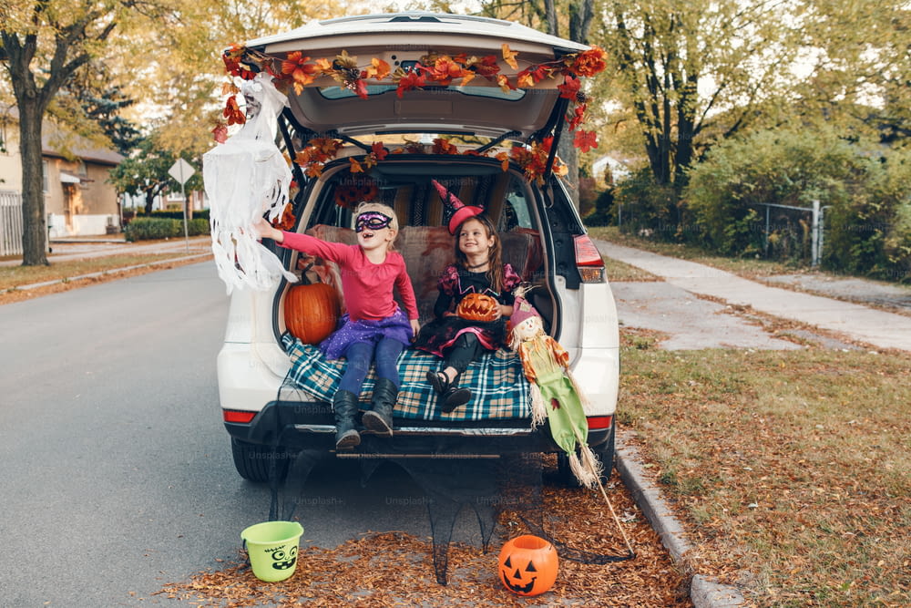 트릭 또는 트렁크. 어린이 형제 자매는 차 트렁크에서 할로윈을 축하합니다. 10 월 휴일 야외를 준비하는 친구 어린이 소녀. 사회적 거리와 안전한 대안 축하.