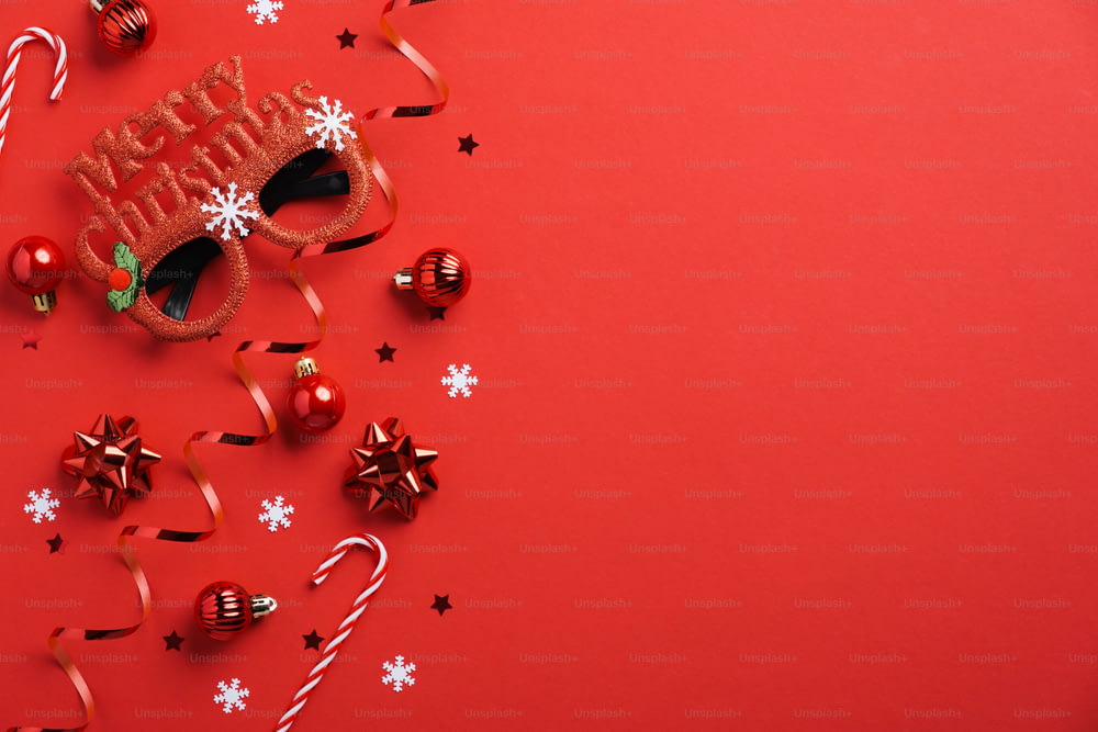 Maqueta de tarjeta de invitación a la fiesta de Navidad. Vasos festivos, decoración de adornos, bastones de caramelo, confeti sobre fondo rojo. Plano plano, vista superior, espacio de copia