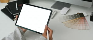 Close up view of young female graphic designer hands holding stylus pen and blank screen tablet on white table.