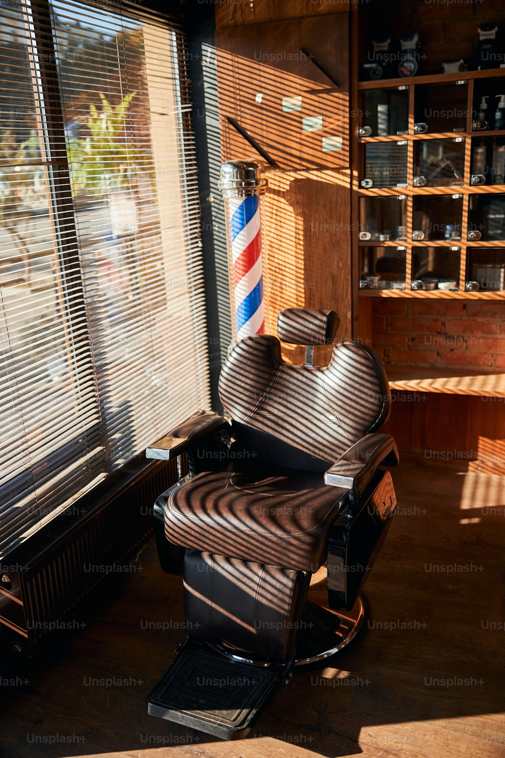 ブラインド付きの窓際にある調節可能なヘッドレスト付きのリクライニングブラウンの革張りの理髪椅子