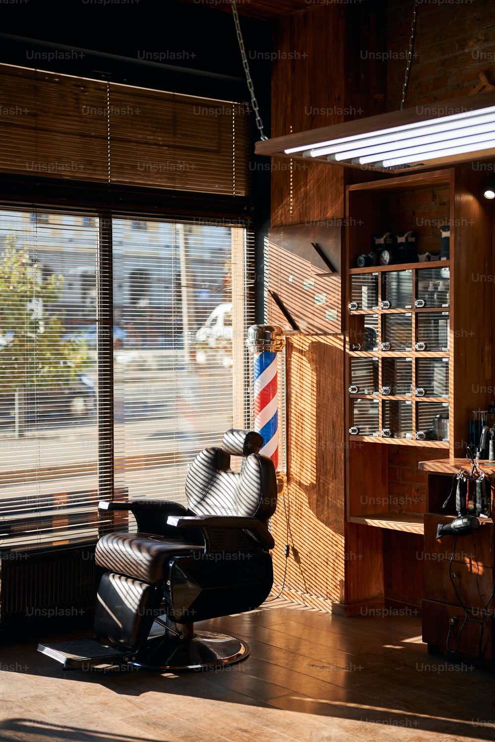 Fauteuil de barbier inclinable en cuir avec appui-tête réglable situé près de la fenêtre avec stores dans un salon de coiffure
