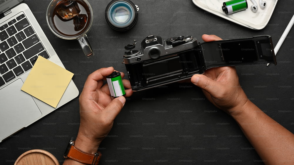 소모품 및 액세서리가 있는 블랙 테이블에 필름 카메라를 사용하는 남성 손의 상위 뷰
