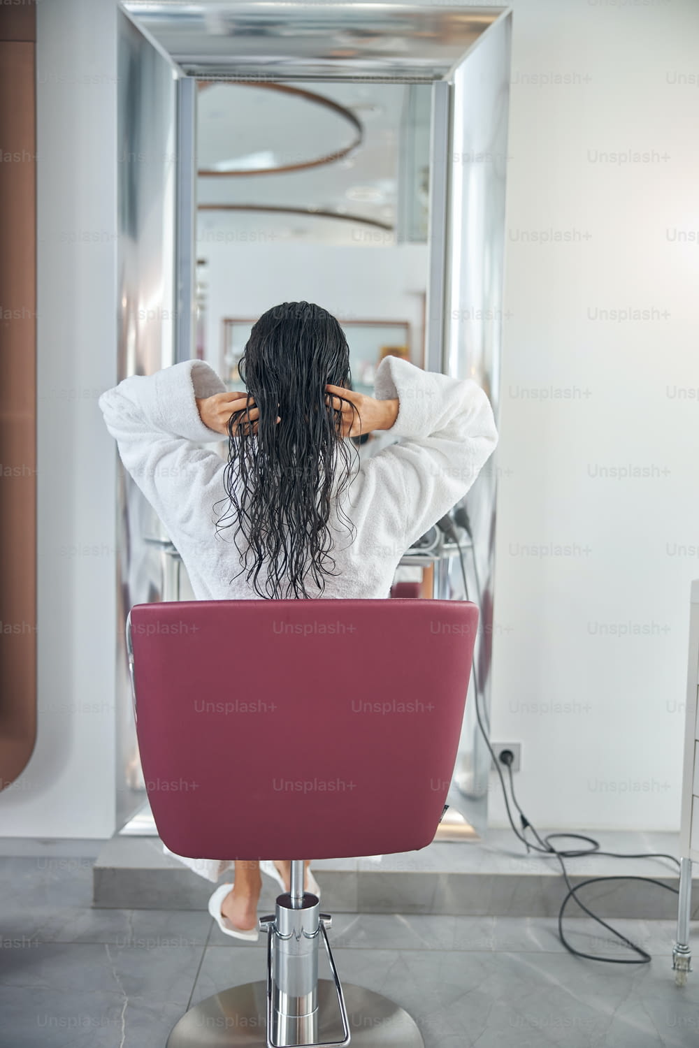Vista traseira da mulher sentada em uma cadeira em um salão de beleza e tocando o cabelo molhado