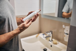 Cropped photo of man hands holding a bottle of cosmetic product near a sink