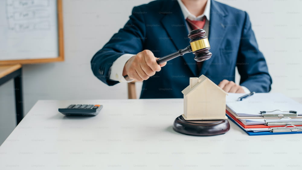 Imagen de un abogado sosteniendo un martillo de subasta en una casa modelo. El concepto de la ley es comprar o vender casas y terrenos, hipotecar.