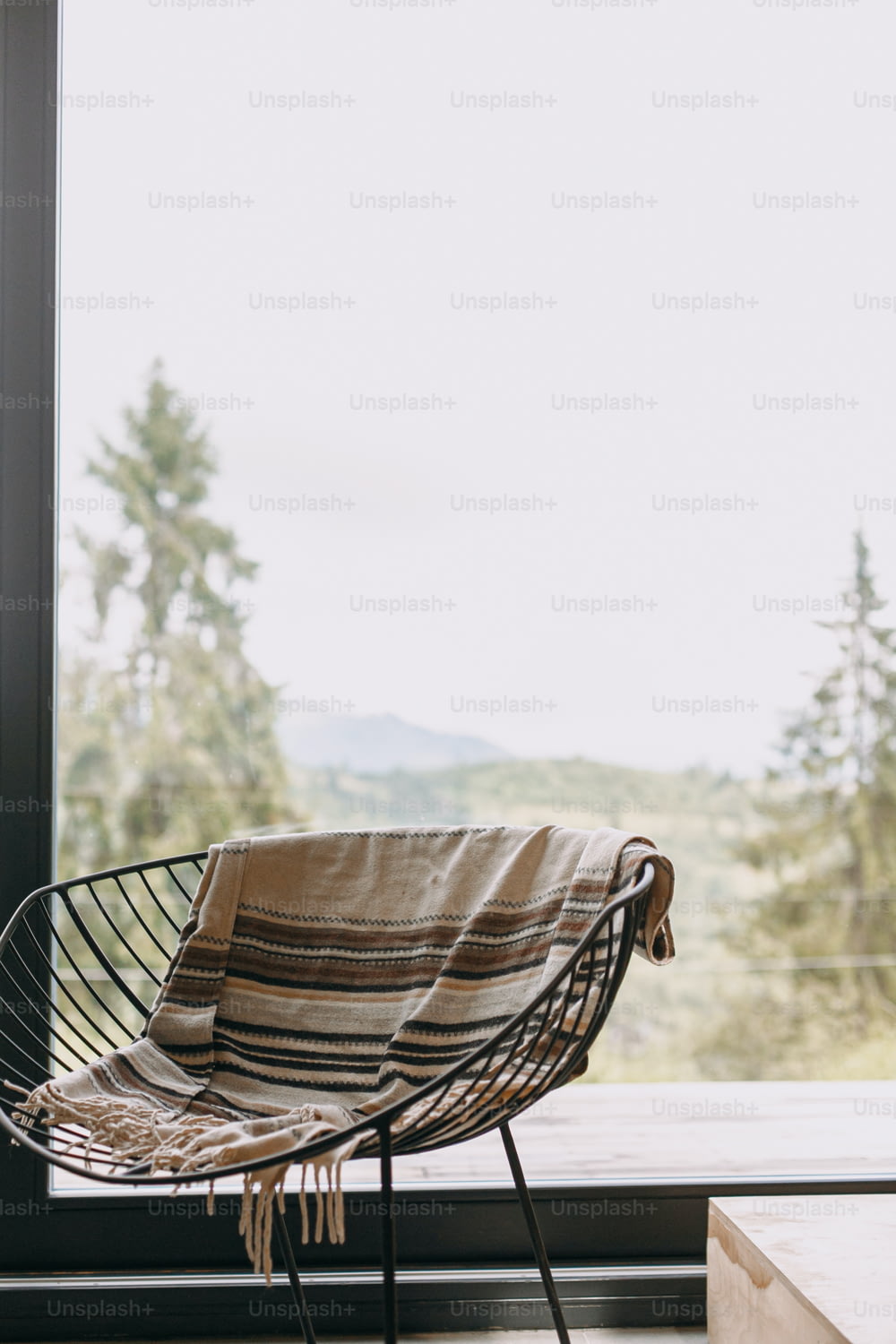 Chaise noire moderne avec couverture douillette et bois de chauffage sur support en métal sur fond de grandes fenêtres avec vue sur les montagnes. Des moments douillets, chaleureux et calmes en cabine à la saison froide.
