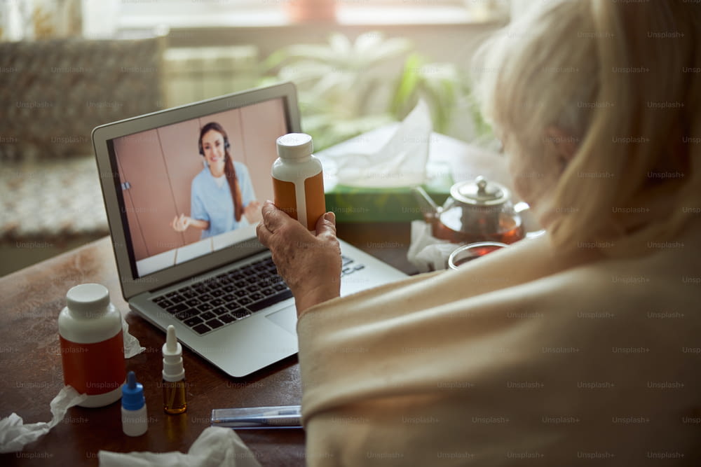 Elderly lady sitting at the table with laptop and discussing medicaments with female physician