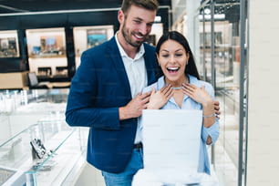 현대 보석 가게에서 쇼핑을 즐기는 아름다운 커플. 젊은 여성은 화려한 목걸이와 귀걸이를 시험해 봅니다.