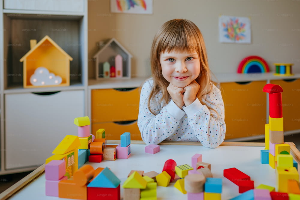 Little 4 years old girl playing with wooden cubes building a toy city