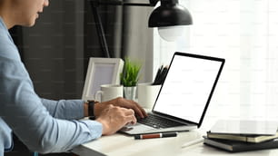 Seitenansicht eines Geschäftsmannes, der an einem Laptop mit leerem Bildschirm an seinem Arbeitsplatz arbeitet.