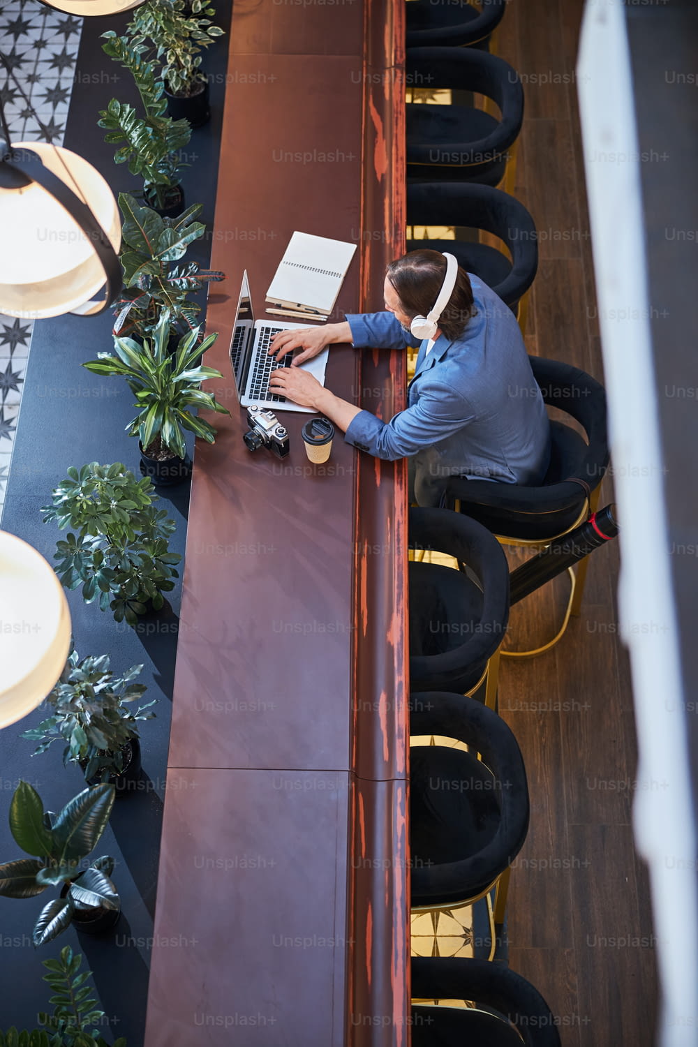 Konzentrierter Mann mit Kopfhörern, der an seinem Laptop zerrt, während er von seinem gemütlichen Hotel aus remote arbeitet