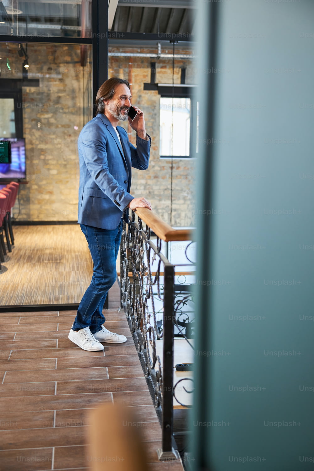Full-length copy space photo of smiley brunette man in blue jacket talking on the phone in hotel hallway