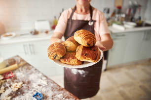 Photo de mise au point sélective d’une assiette avec des croissants tenue par une dame en tablier