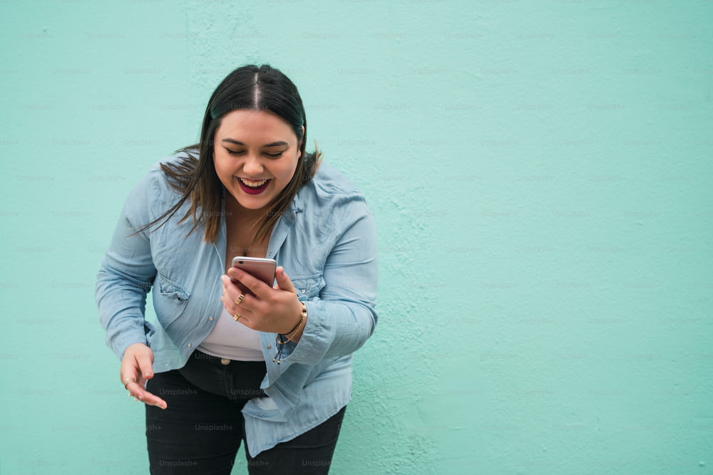 Portrait of young plus size woman smiling while typing text message on her mobile phone outdoors. Technology concept.