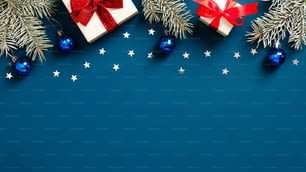 Christmas and New Year banner with fir branches, white gift boxes with red ribbon bows and Christmas balls on dark blue background. Flat lay, top view.