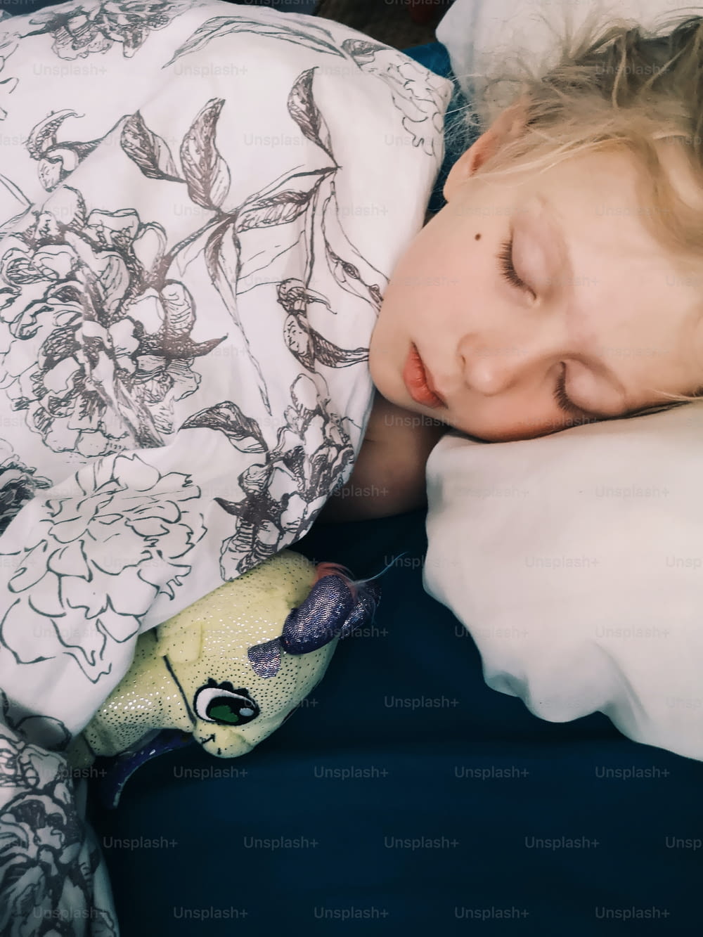 귀여운 사랑스러운 어린 소녀가 집에서 침대에서 좋아하는 장난감을 가지고 자고 있습니다. 수면 노리개 보조 장난감과 함께 꿈을 꾸며 자는 아이. 좋은 꿈꾸세요.