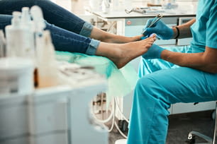 Ritratto di testa ritagliata di paziente non riconosciuto seduto sulla sedia medica mentre il medico in chiodi di garofano blu esamina i piedi nel centro di bellezza