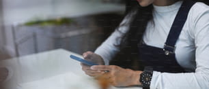 Una joven freelancer sentada en su estación de trabajo y usando un teléfono inteligente.