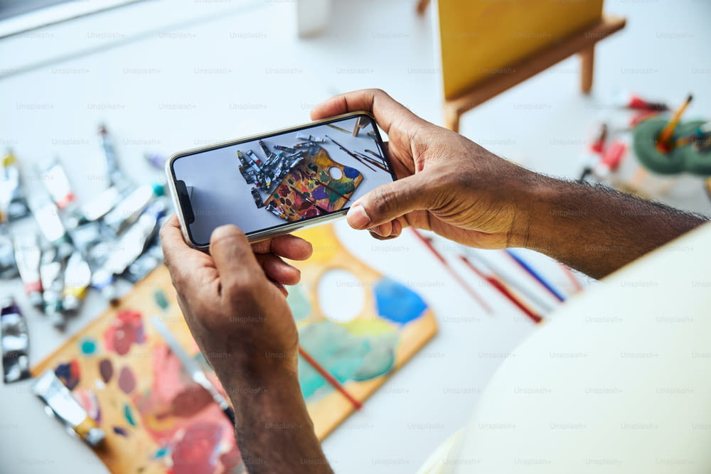 Uomo con uno smartphone che scatta una foto di una tavolozza di colori sdraiata sul tavolo