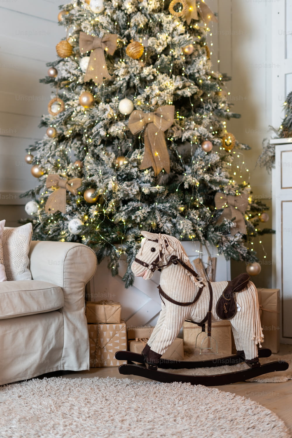 Vertical photo of cozy living room with rocking horse and christmas presents near decorated new year tree. Contemporary interior design with rug and sofa in modern apartment