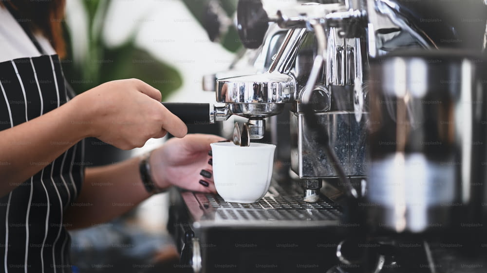 Vista de cerca de las manos del barista usando la máquina de café para hacer café en la cafetería.