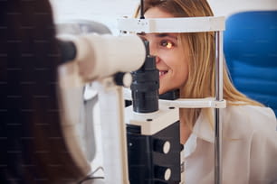 Ritratto ravvicinato di vista laterale di bella femmina sorridente che guarda la macchina della lampada di slittamento nell'armadio dell'optometrista