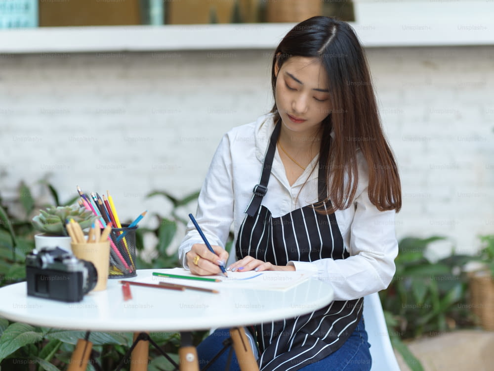Portrait of of female artist with apron painting with coloured pencil on coffee table in garden