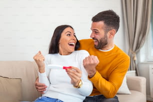 Shot of a happy young couple taking a pregnancy test at home. A Happy excited woman making positive pregnancy test and celebrating. Excited woman getting pregnant. Couple Celebrating Positive Home Pregnancy Test Result