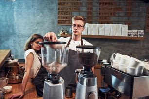 Behind the coffee machine. Two young workers indoors. Conception of business and service.