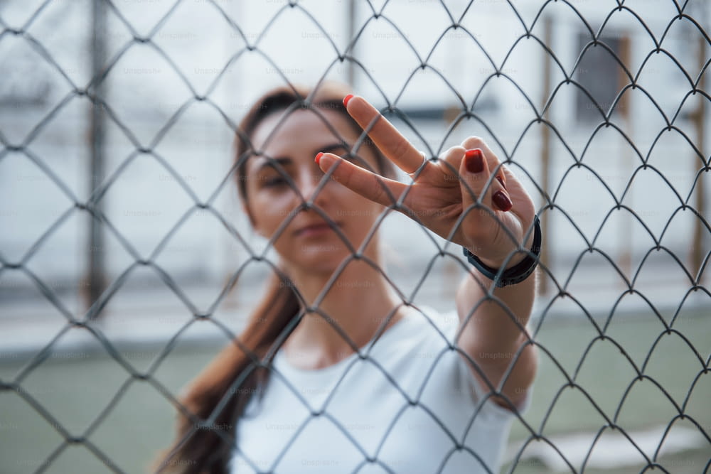 Brunette si trova dietro la recinzione e mostra il gesto usando due dita.