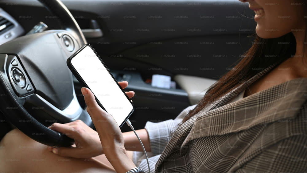 Plan recadré d’une jeune femme tenant un smartphone avec un écran défaillant tout en conduisant une voiture.