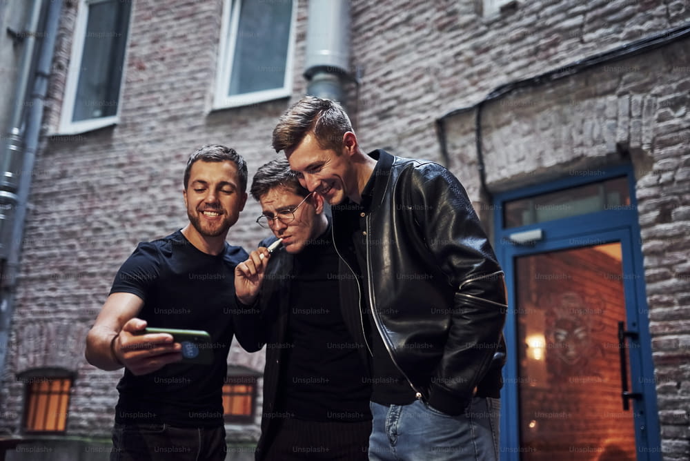 Three male friends stands outside the bar. Having conversation. In nice clothes.