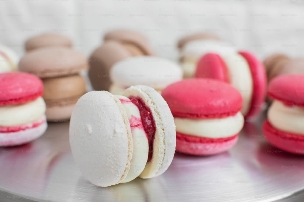 Close up of colorful white, red, and caramel chocolate macarons dessert, filling with tasty ganache, on the table at light kitchen or confectionery shop.